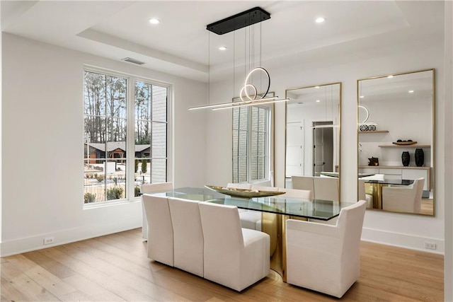 dining room featuring a chandelier, light wood-type flooring, and a tray ceiling