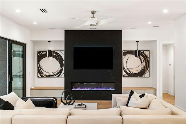 living room with ceiling fan, a high end fireplace, and light hardwood / wood-style flooring