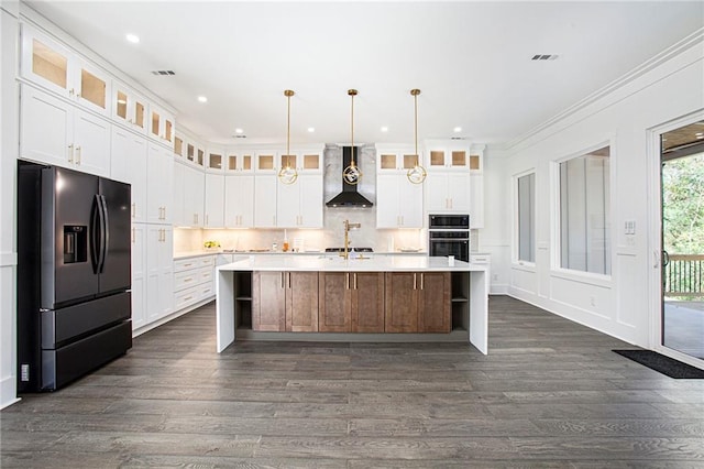 kitchen featuring a spacious island, black appliances, white cabinets, and wall chimney range hood