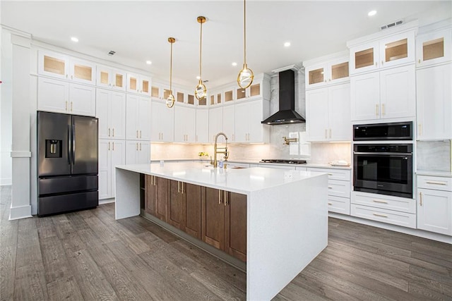 kitchen featuring wall chimney range hood, appliances with stainless steel finishes, sink, an island with sink, and white cabinets