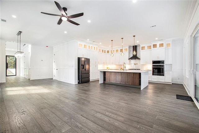 kitchen with wall chimney range hood, appliances with stainless steel finishes, a large island with sink, and dark hardwood / wood-style floors