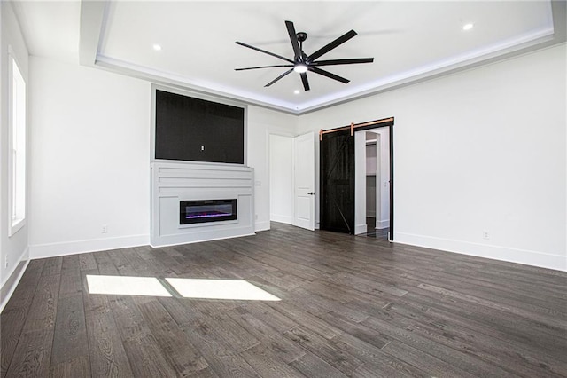 unfurnished living room featuring dark wood-type flooring, a barn door, and ceiling fan