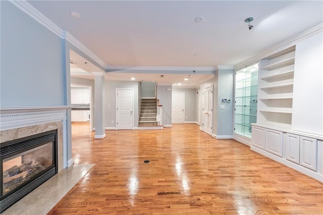 unfurnished living room featuring light hardwood / wood-style flooring, crown molding, a fireplace, and built in features