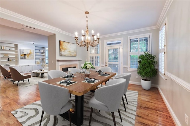 dining area with ornamental molding, a chandelier, built in features, and light wood-type flooring