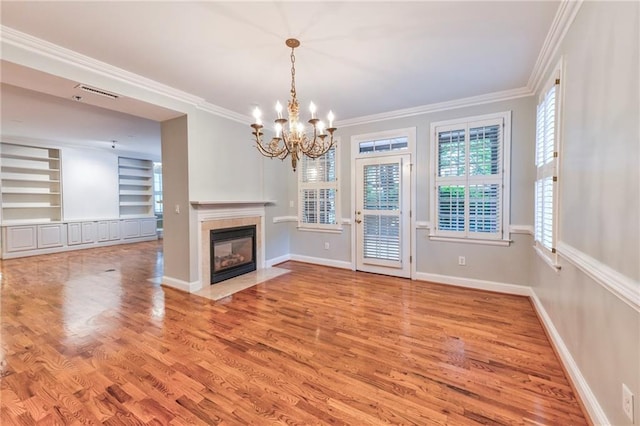 unfurnished living room with hardwood / wood-style floors, a fireplace, a chandelier, crown molding, and built in shelves