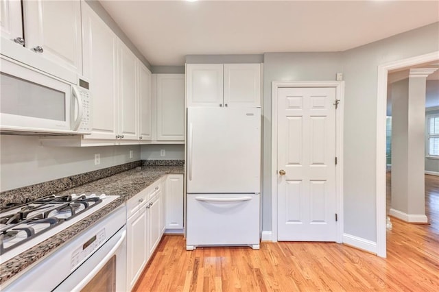 kitchen with dark stone countertops, white cabinets, white appliances, and light hardwood / wood-style flooring