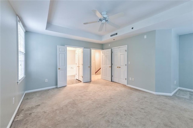 unfurnished bedroom featuring light carpet, a tray ceiling, and ceiling fan