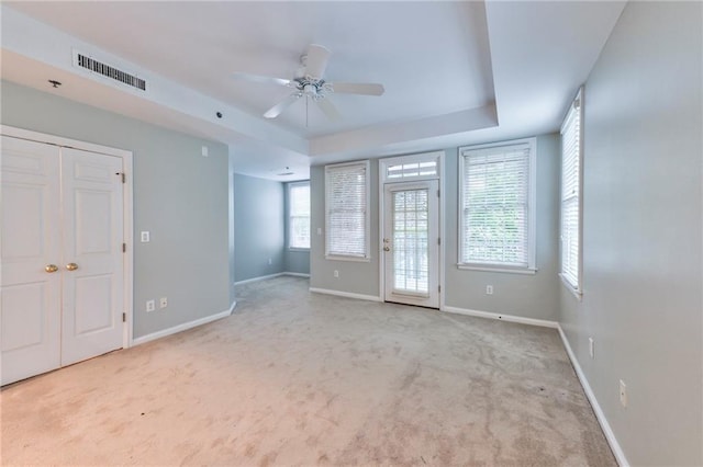 spare room featuring a tray ceiling, light colored carpet, and ceiling fan