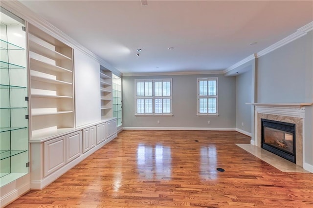 unfurnished living room with built in shelves, a fireplace, ornamental molding, and light hardwood / wood-style floors