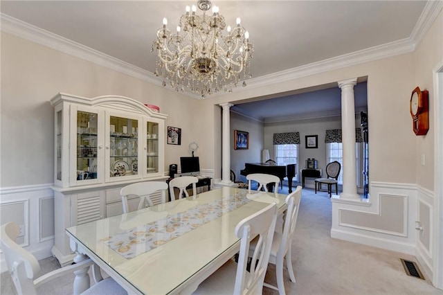 carpeted dining space featuring decorative columns, ornamental molding, and a chandelier