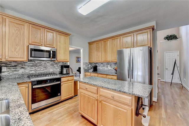 kitchen featuring light stone counters, light brown cabinetry, light wood-type flooring, and appliances with stainless steel finishes