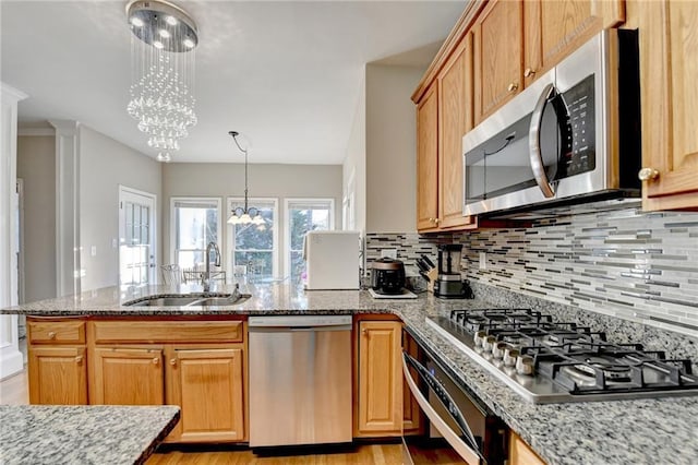 kitchen featuring sink, stainless steel appliances, a notable chandelier, light stone countertops, and decorative light fixtures