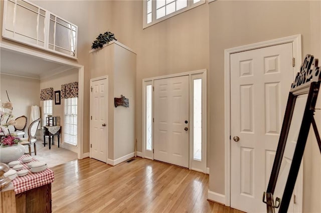 foyer entrance featuring crown molding, a towering ceiling, plenty of natural light, and light hardwood / wood-style flooring