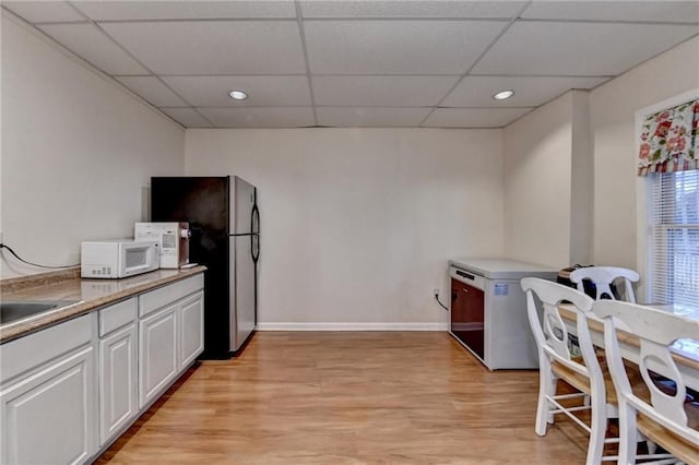 kitchen with refrigerator, white cabinetry, stainless steel fridge, light hardwood / wood-style floors, and a drop ceiling