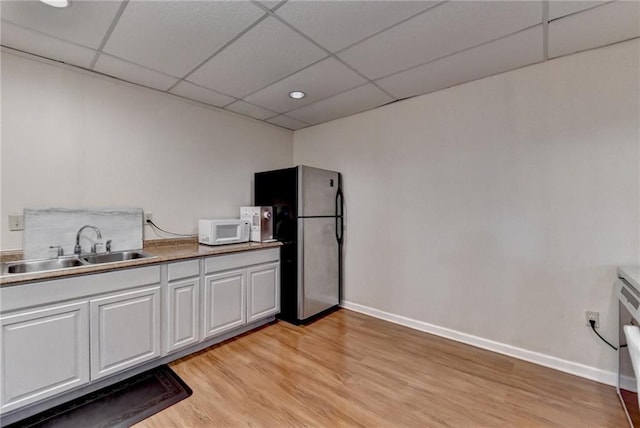 kitchen with sink, stainless steel fridge, light hardwood / wood-style floors, white cabinets, and a drop ceiling