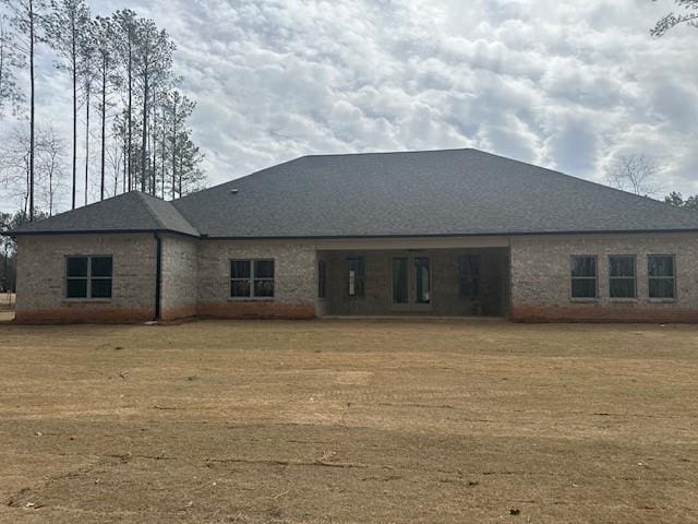 rear view of property featuring an attached garage, roof with shingles, and a yard