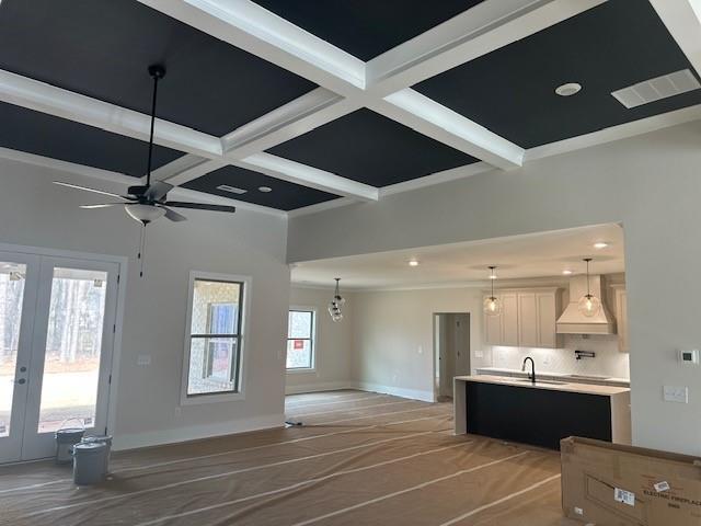 unfurnished living room featuring ceiling fan, coffered ceiling, baseboards, french doors, and beam ceiling