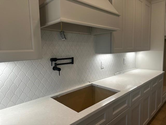 kitchen with tasteful backsplash, a sink, and custom range hood