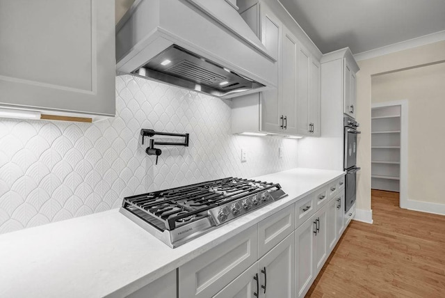 125 Drummond Pl, Covington, GA 30014 - kitchen with stainless steel gas stovetop, light countertops, custom range hood, light wood-style flooring, and ornamental molding
