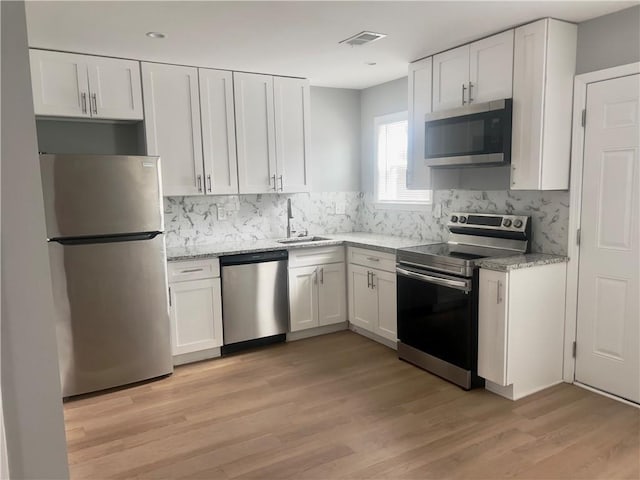 kitchen with sink, white cabinets, light stone counters, light hardwood / wood-style floors, and stainless steel appliances