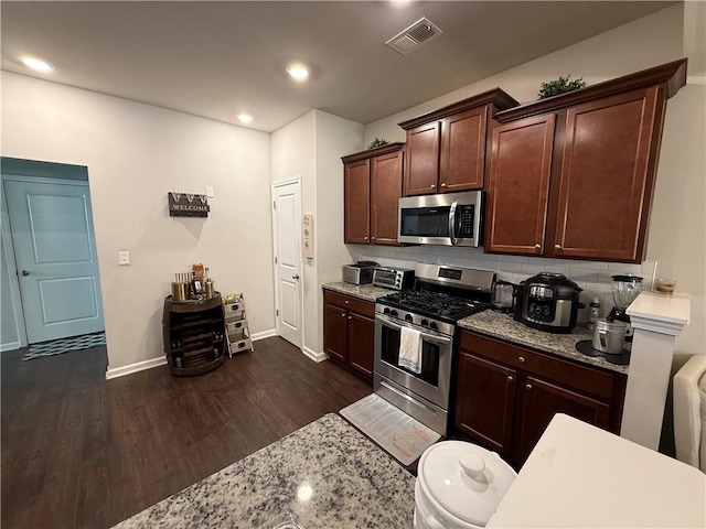 kitchen featuring stainless steel appliances, light stone countertops, decorative backsplash, dark brown cabinetry, and dark wood-type flooring