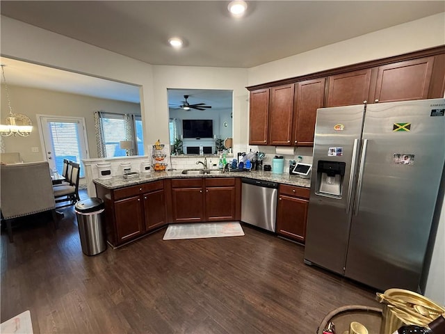 kitchen featuring light stone counters, dark wood-type flooring, pendant lighting, ceiling fan with notable chandelier, and appliances with stainless steel finishes