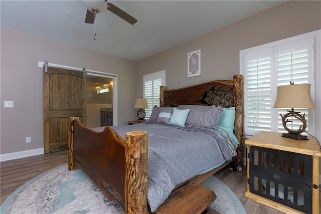 bedroom with ensuite bath, wood finished floors, a barn door, baseboards, and ceiling fan