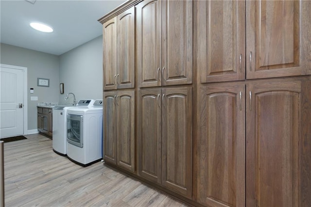 washroom with cabinet space, baseboards, light wood finished floors, and washer and clothes dryer