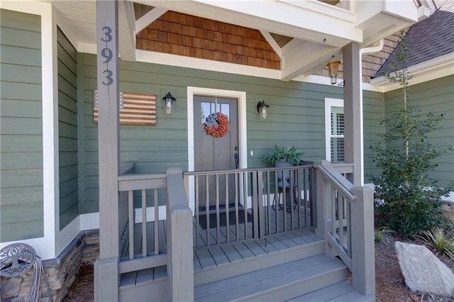 doorway to property featuring covered porch and a shingled roof