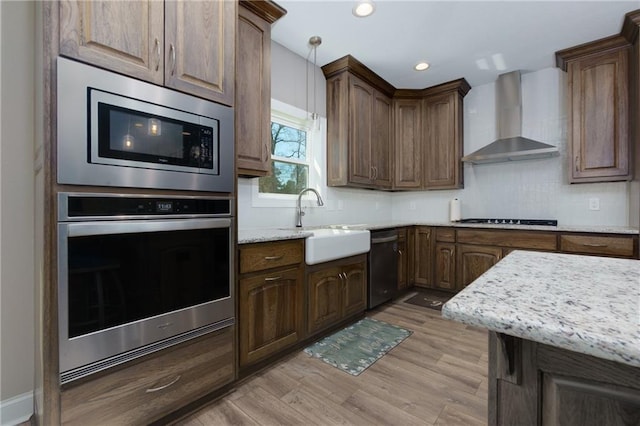 kitchen featuring light wood-type flooring, a sink, backsplash, appliances with stainless steel finishes, and wall chimney exhaust hood