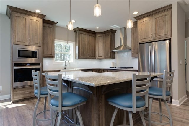 kitchen with light wood-style flooring, appliances with stainless steel finishes, a center island, and wall chimney exhaust hood