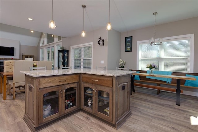 kitchen featuring light stone counters, light wood-type flooring, glass insert cabinets, and vaulted ceiling