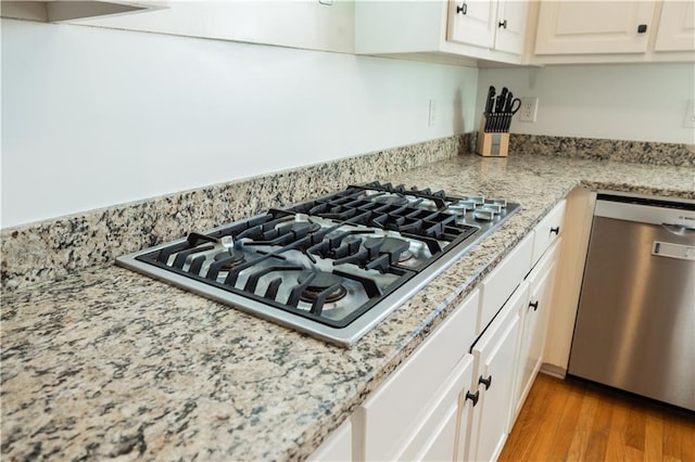 kitchen with white cabinets, light wood-type flooring, light stone countertops, and stainless steel appliances