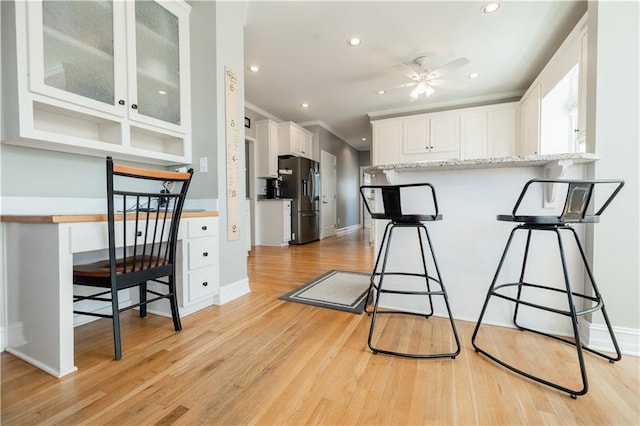 kitchen with white cabinetry, light hardwood / wood-style floors, stainless steel fridge with ice dispenser, kitchen peninsula, and a breakfast bar area