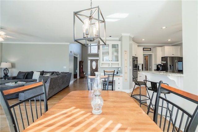 dining space with ceiling fan with notable chandelier, light hardwood / wood-style flooring, and crown molding