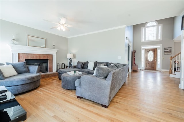 living room featuring ornamental molding, ceiling fan, a brick fireplace, and light hardwood / wood-style flooring