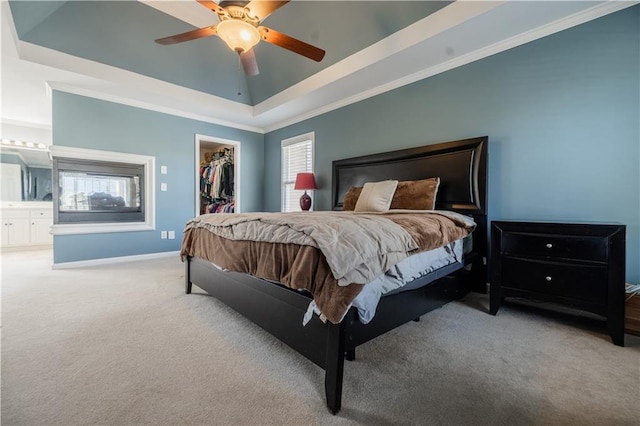 bedroom featuring ceiling fan, ensuite bath, a walk in closet, and a raised ceiling