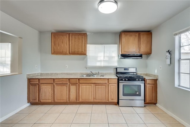 kitchen with light stone counters, sink, light tile patterned floors, and stainless steel gas range