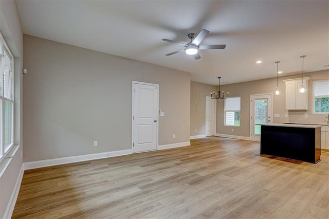 unfurnished living room with ceiling fan with notable chandelier and light hardwood / wood-style floors