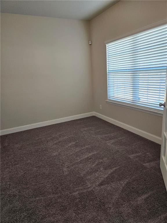 spare room featuring dark colored carpet and baseboards