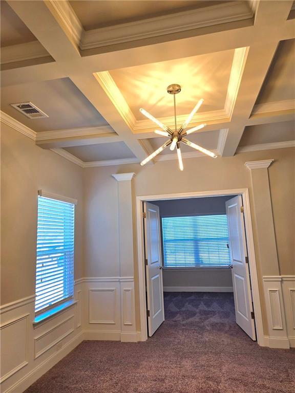 spare room featuring visible vents, dark carpet, coffered ceiling, and a decorative wall