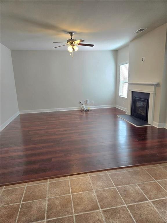 unfurnished living room with visible vents, baseboards, a glass covered fireplace, dark wood-style floors, and ceiling fan