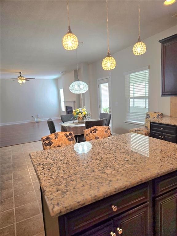 kitchen with light stone counters, a kitchen island, open floor plan, dark brown cabinets, and decorative light fixtures