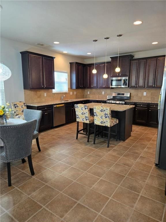 kitchen featuring dark brown cabinets, appliances with stainless steel finishes, pendant lighting, and a breakfast bar area