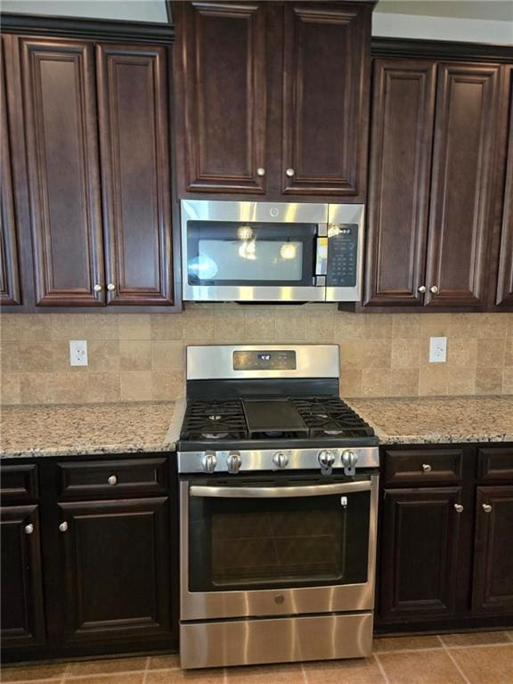 kitchen with dark brown cabinetry, light stone countertops, appliances with stainless steel finishes, and decorative backsplash