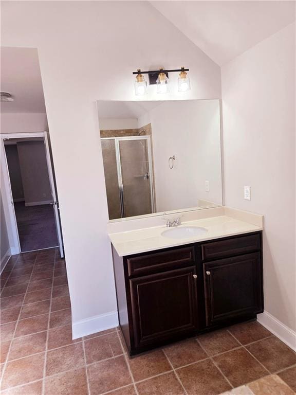 bathroom with a stall shower, vaulted ceiling, vanity, baseboards, and tile patterned floors