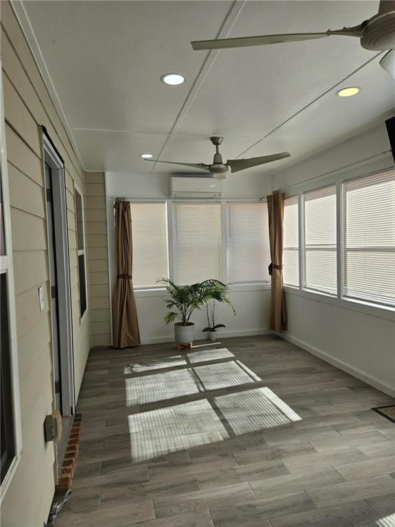 unfurnished sunroom featuring ceiling fan and a wall mounted air conditioner