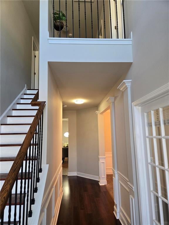 corridor with dark wood-style floors, a high ceiling, ornate columns, and stairs