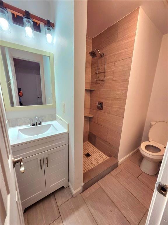 bathroom with tiled shower, vanity, and toilet