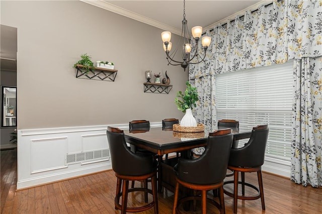 dining area with ornamental molding, hardwood / wood-style flooring, a chandelier, and a wainscoted wall